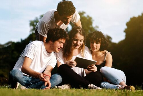 Vier SchülerInnen sitzen auf der Wiese und schauen in ein Tablet