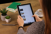 Frau sitzt beim Tisch und surft am Tablet im Internet.